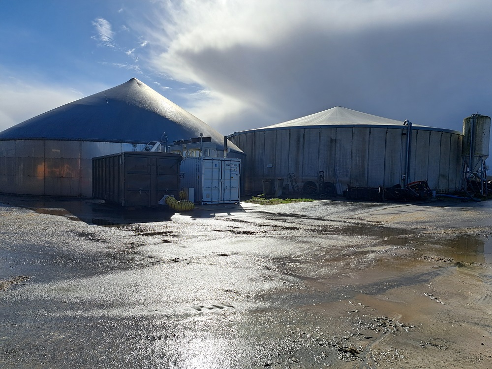 Links de mestvergister, rechts de silo waar het digestaat in gaat. Daarvoor links een container waarin producten kunnen worden gedroogd met restwarmte van de generatoren. Rechts de container met daarin de generatoren met alle benodigdheden die daarbij horen. 